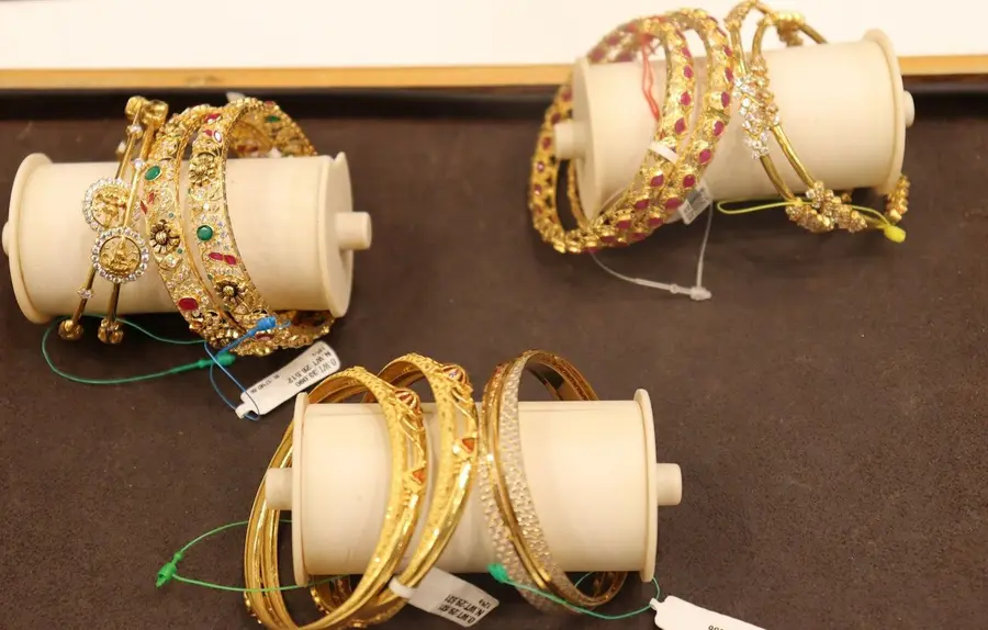 Rolls of gold bangles on white cylinders over brown velvet, tagged.