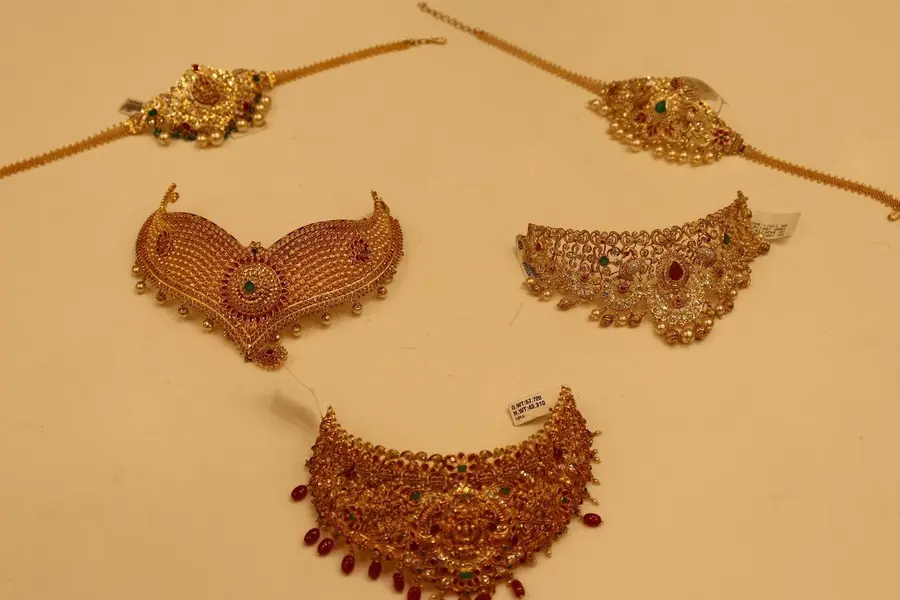 A bridal set laid out flat on cream: maang tikkas above, a gold mesh choker, a kundan choker and a ruby fringe choker below.